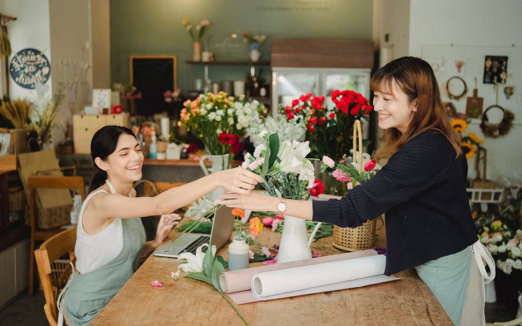 Two smiling women in a floral shop creating beautiful bouquets and arrangements.
